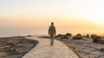 Rear view of a person on a stone path leading to a golden horizon. Rocky ground behind symbolizes past challenges, emphasizing hope.