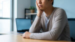 Un homme, la main sous le menton, semble fatigué ou las devant son ordinateur portable au bureau, un signe de burn-out.