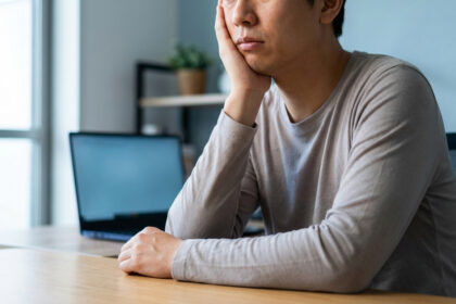 Un homme, la main sous le menton, semble fatigué ou las devant son ordinateur portable au bureau, un signe de burn-out.