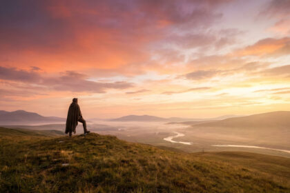 Personne debout sur une colline dominant une vallée brumeuse au lever du soleil.